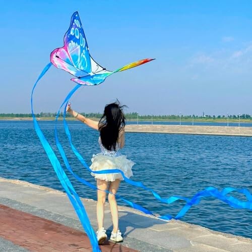 Girl flying a colorful butterfly kite by the water.